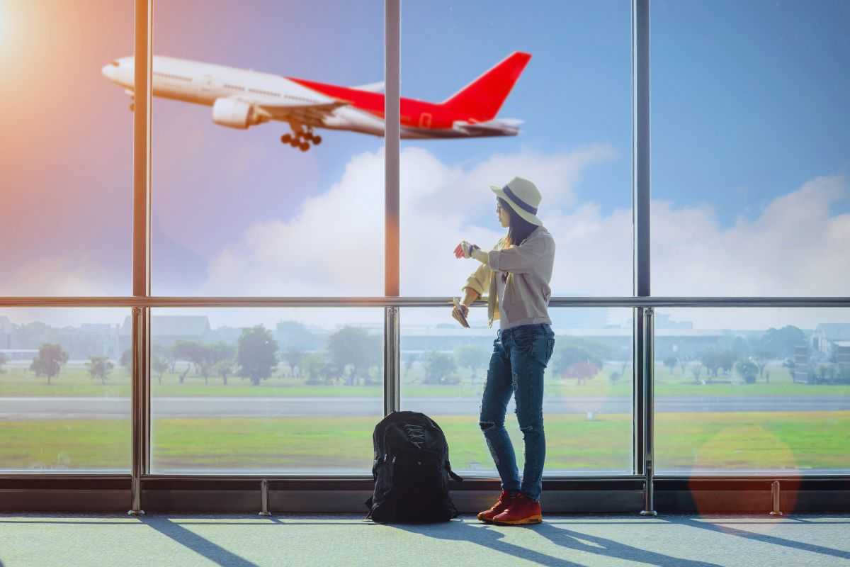 Donna in aeroporto che controlla orario e vede aereo in partenza