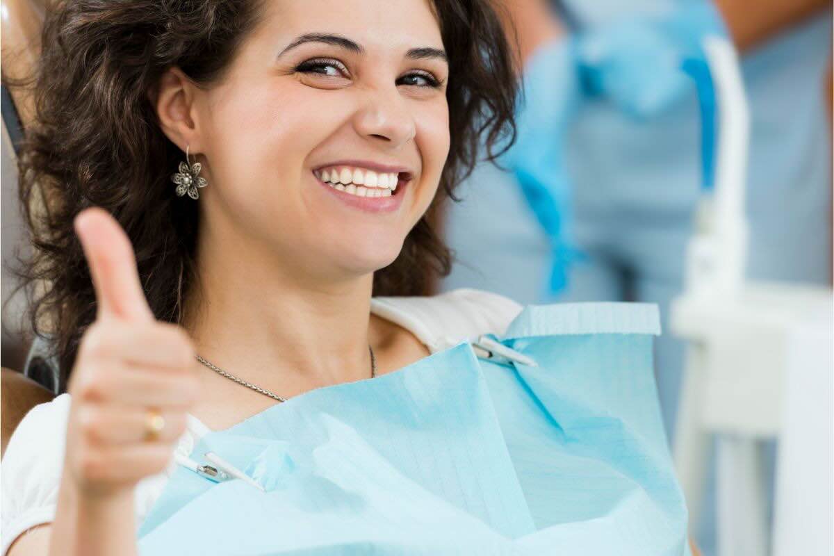 Donna con pollice in su, sorriso smagliante dal dentista