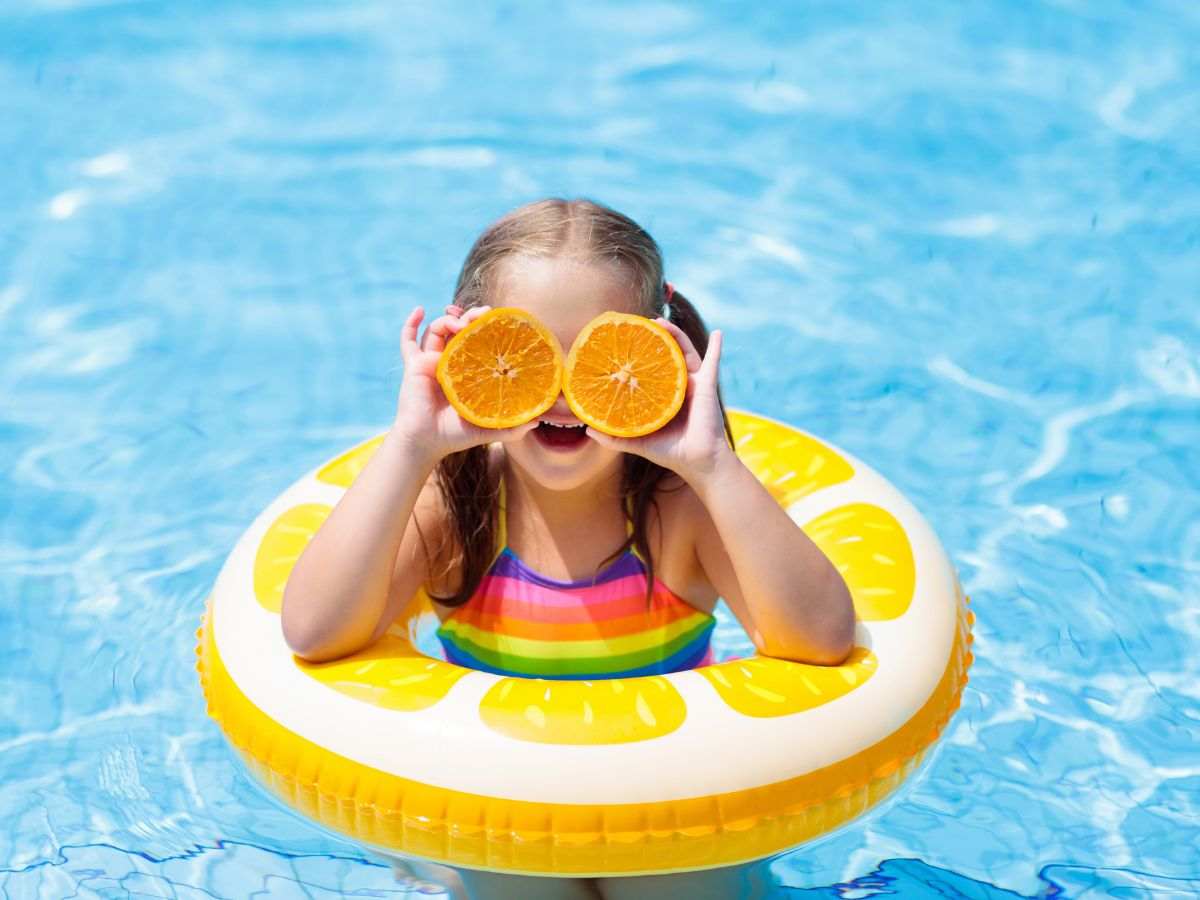 Bambina dentro ciambella in piscina con arance su occhi