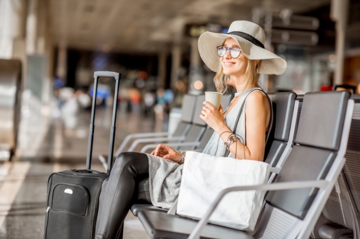 donna con cappello in aeroporto con valigia e caffè